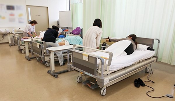 受講者の看護師さんが患者役になり、看護大学の臨床用ベッドで側臥位の下肢の施術を学ぶ